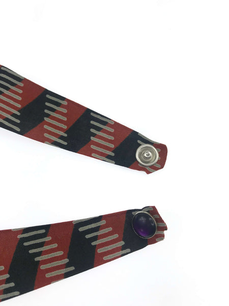 Close-up of a handmade fabric bracelet with a bold burgundy, black, and gray geometric pattern, featuring a secure snap closure and an accent purple gem detail. Perfect for adding a touch of unique, artisanal style to any outfit.