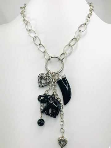 Close-up of a bold silver-tone charm necklace with oversized oval links, featuring a polished black tusk, an intricately detailed elephant charm, and silver heart pendants. Lightweight and stylish, this necklace includes a matching fish hook clasp, perfect for both casual and formal occasions.